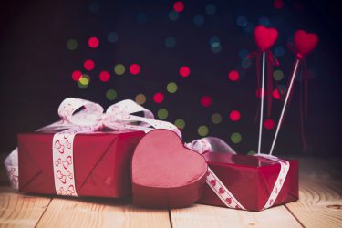 Gifts in red boxes for Valentine's day. Red heart on a wooden table against the background of colorful bokeh.